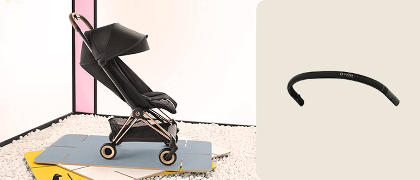 Ein eleganter schwarzer Kinderwagen mit einem Verdeck auf einer blauen Matte, neben einem gebogenen schwarzen Lenker auf beigem Hintergrund.