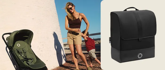 Eine Frau mit Sonnenbrille spaziert mit einem Kind in der Nähe eines Leuchtturms. Sie schiebt einen grünen Kinderwagen. Rechts ist ein schwarzer Rucksack zu sehen.