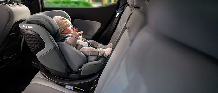 Ein Baby in einem gemütlichen Kindersitz, das eine Strickmütze und warme Kleidung trägt und sicher auf dem Rücksitz eines Fahrzeugs angeschnallt ist.