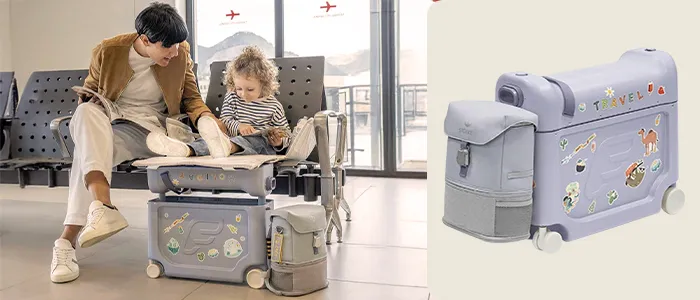 Ein Erwachsener und ein Kind sitzen auf einem Koffer im Flughafen und schauen in ein Buch. Der Koffer hat Rollen und Aufkleber mit Reisemotiven.