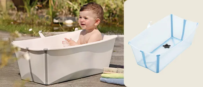 Ein Baby sitzt im Freien in einer weißen, zusammenklappbaren Badewanne. Daneben steht eine leere, blaue Version dieser Badewanne.