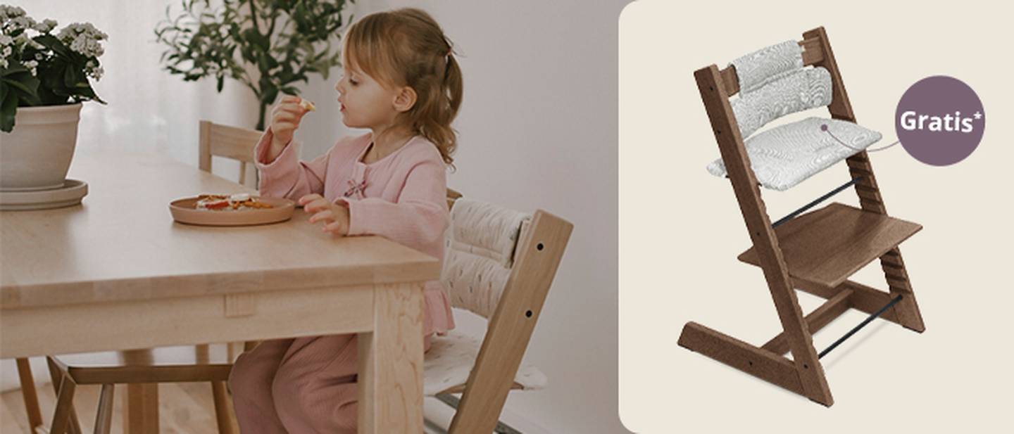 Ein Kind in einem rosa Outfit sitzt auf einem Stokke Tripp Trapp Hochstuhl und isst. Hinweis auf Gratis Sitzkissen