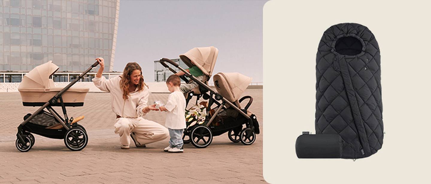 Frau kniet mit Kleinkind zwischen zwei beigen Kinderwagen auf dem Bürgersteig; im rechten Bildausschnitt ist ein schwarzer, gesteppter Fußsack für den Kinderwagen zu sehen.