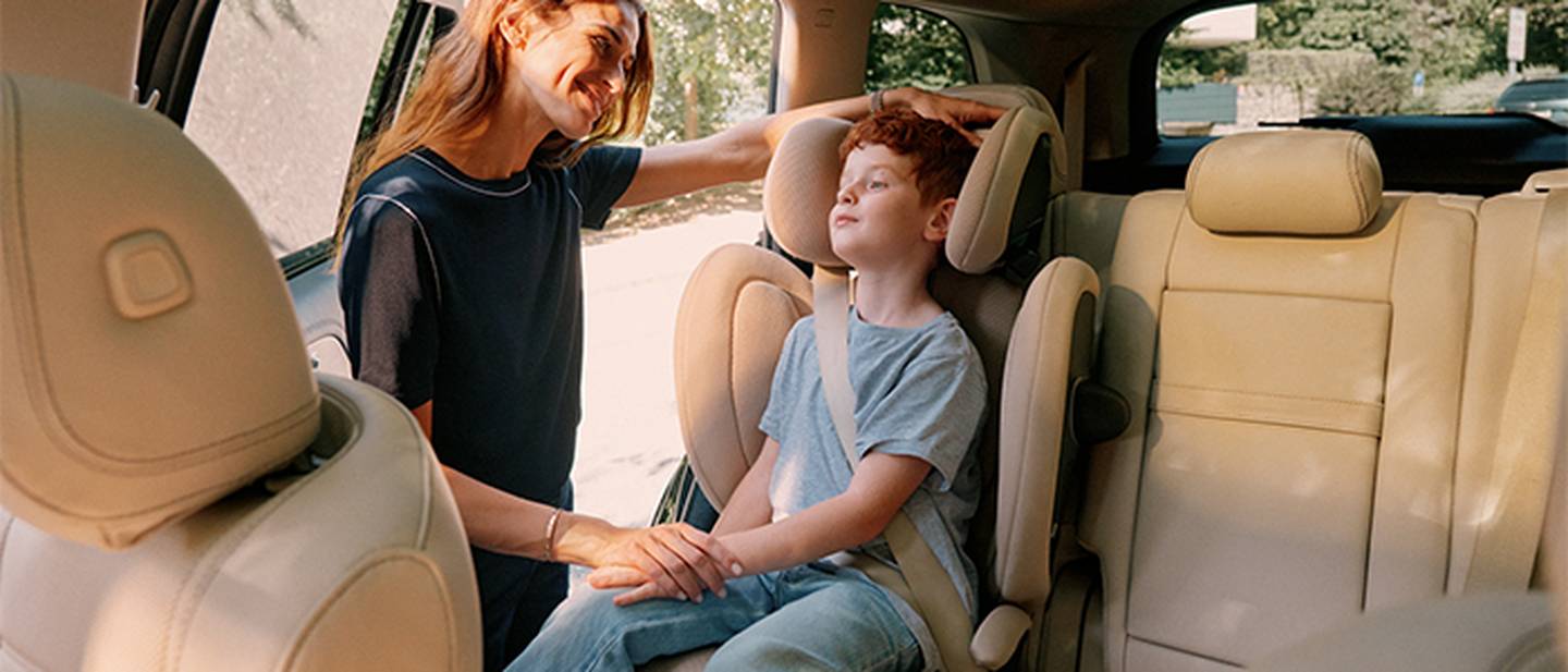 Eine Frau lächelt ein Kind an, das in einem Autositz sitzt, während das Sonnenlicht durch die Fenster strömt.