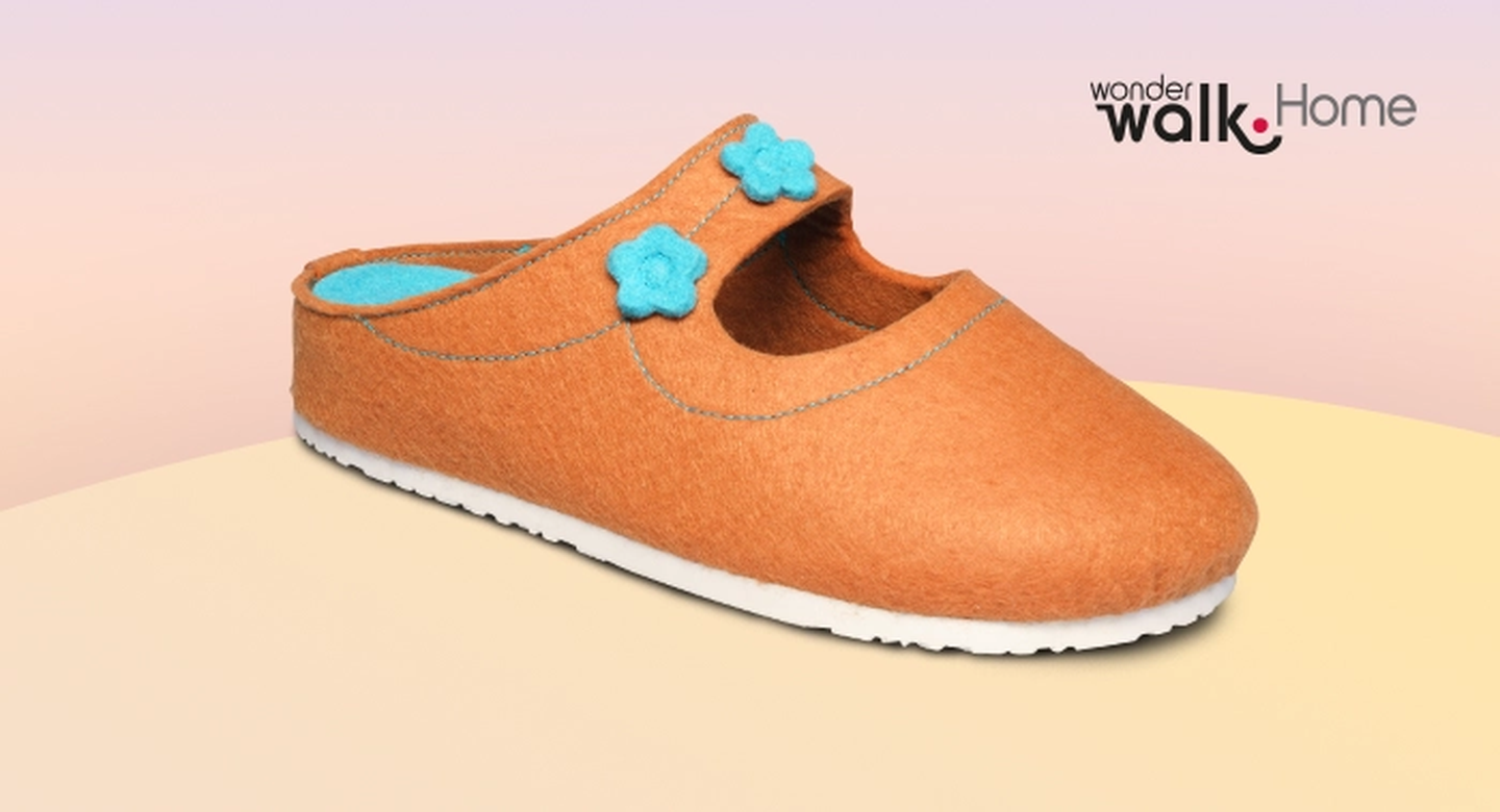 Ein orangefarbener Filzpantoffel mit blauen Blumenverzierungen und weißer Sohle vor einem Hintergrund mit Farbverlauf und dem Schriftzug „Wonder Walk. Home”.