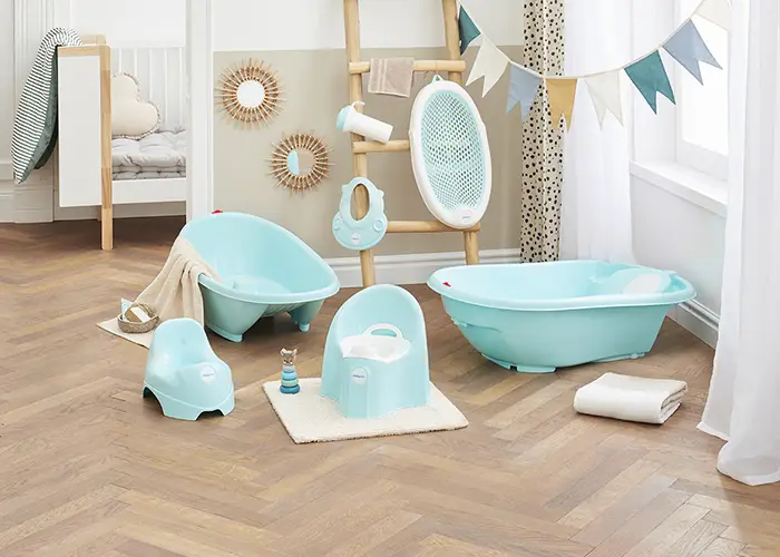 Ein Kinderzimmer mit aquafarbenen Baby-Badeutensilien, einschließlich Wanne, Töpfchen und Zubehör, auf einem Holzboden. Wimpel und Dekoration hängen an den Wänden.