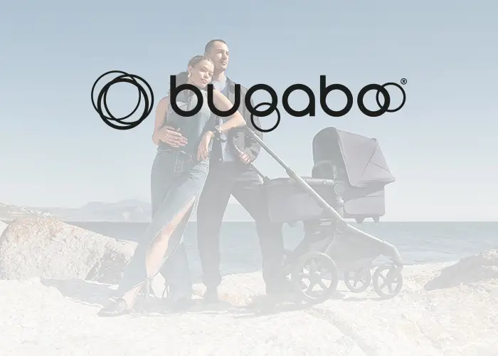 Ein Paar steht mit einem Kinderwagen an einem felsigen Strand unter klarem Himmel. Das Bugaboo-Logo ist prominent über ihnen zu sehen.