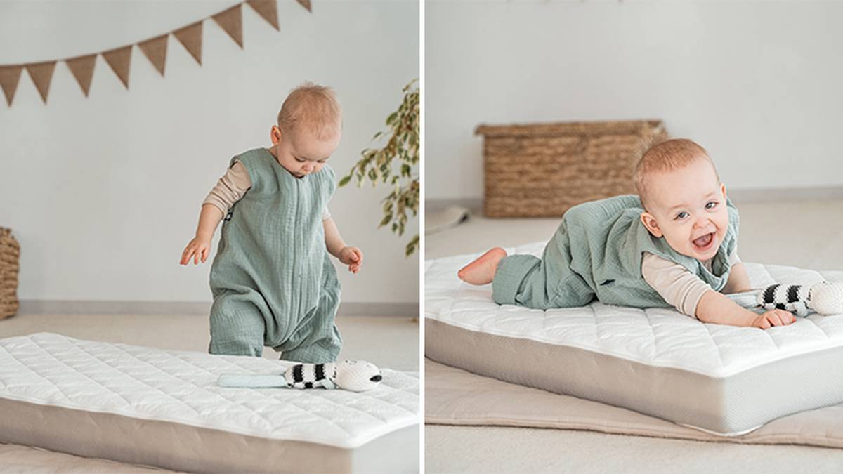Ein Baby in einem grünen Outfit steht und krabbelt auf einer Matratze mit einem Spielzeug; im Hintergrund ist eine dekorierte Wand und ein Weidenkorb zu sehen.