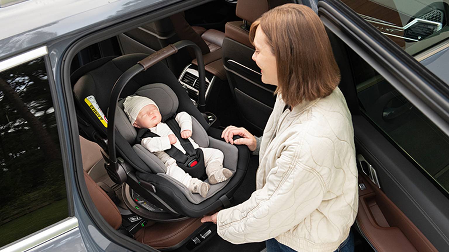 Eine Frau sichert ein schlafendes Baby in einem rückwärtsgerichteten Kindersitz im Auto. Das Baby trägt eine Strickmütze.