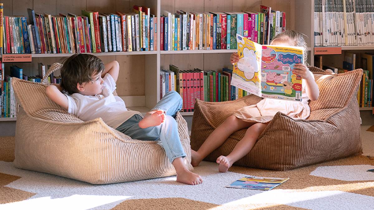 Zwei Kinder sitzen auf Sitzsäcken in einer Bibliothek. Das eine liest ein „Peppa Pig“-Buch, während das andere sich entspannt, hinter ihnen ein Bücherregal.