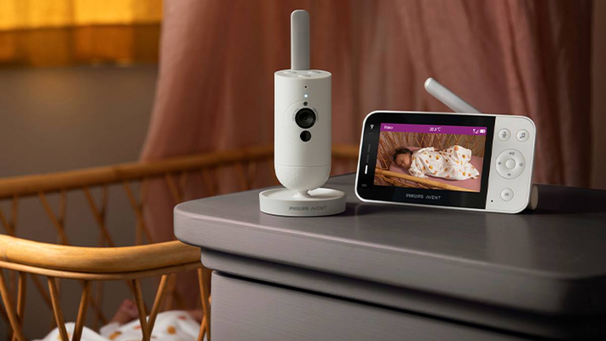 Auf einem Tisch steht ein Babyphone, das ein schlafendes Baby zeigt. Die Kamera des Babyphones ist in der Nähe eines Kinderbetts positioniert und erfasst die Szene im Kinderzimmer.