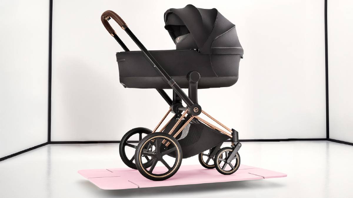 Schwarzer Kinderwagen mit kupferfarbenen Details, elegantem Design, großen Rädern und einer rosa Matte darunter, vor weißem Hintergrund.