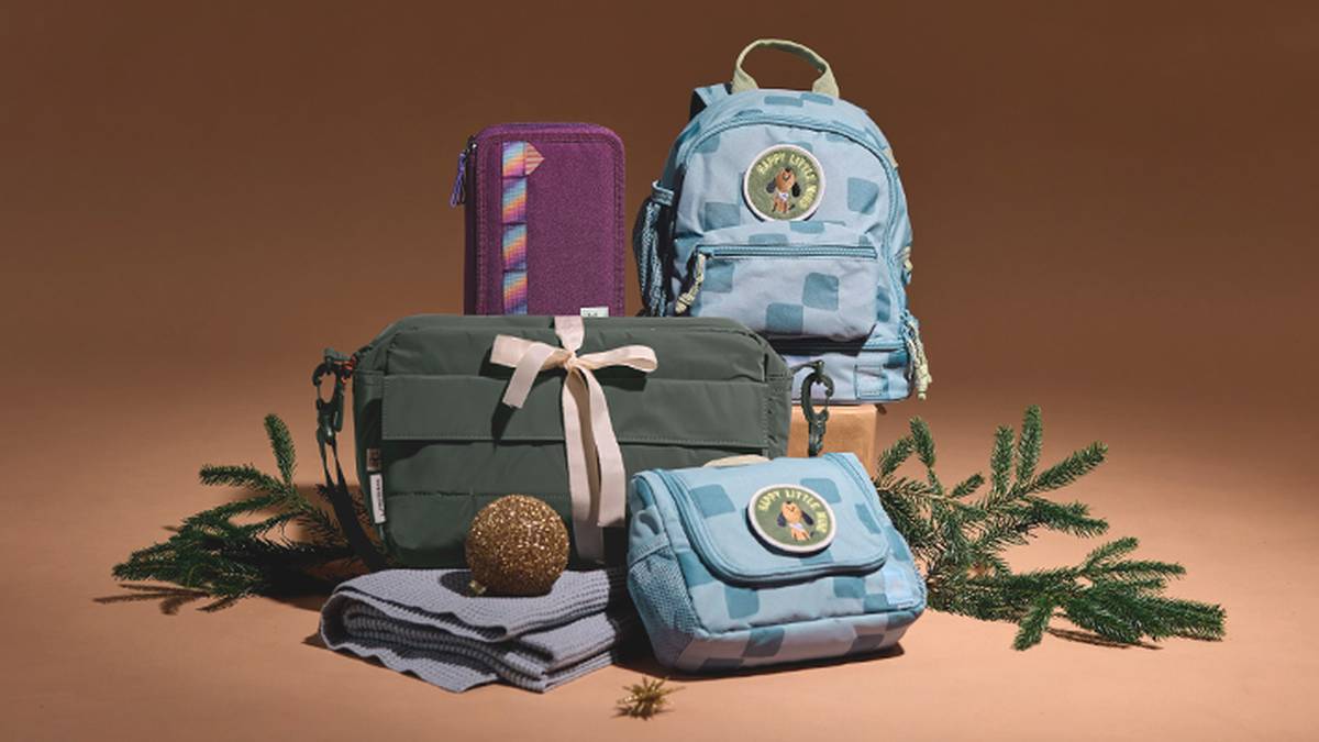 Verschiedene Reisetaschen auf braunem Hintergrund mit Kiefernzweigen: grüne Reisetasche mit Schleife, blauer gemusterter Rucksack und Beutel, lila Koffer, goldener Schmuck.