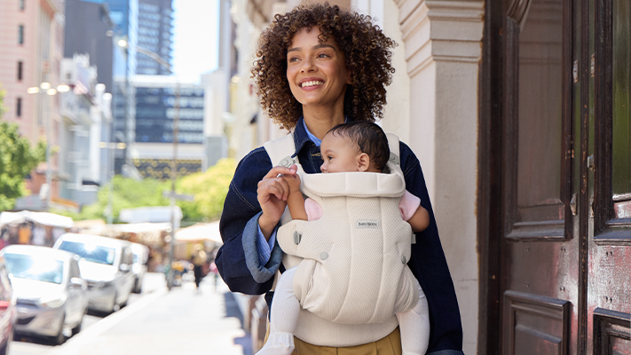Eine Frau läuft mit einem Baby in einer Babytrage durch die Stadt.