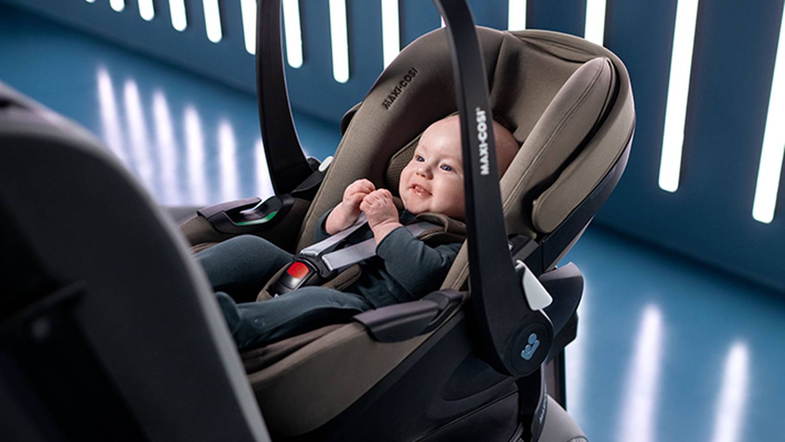 Ein lächelndes Baby sitzt in einem grau-schwarzen Autositz, umgeben von vertikalen Lichtlinien auf blauem Grund.