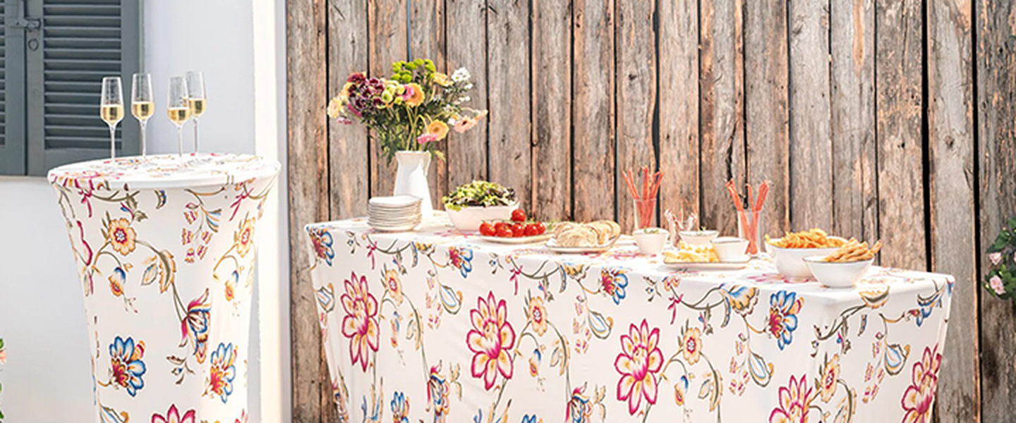 Ein mit Blumenmuster gestaltetes Tischarrangement mit Vorspeisen, kleinen Tellern, Blumen und Champagnergläsern vor einem rustikalen Holzhintergrund.