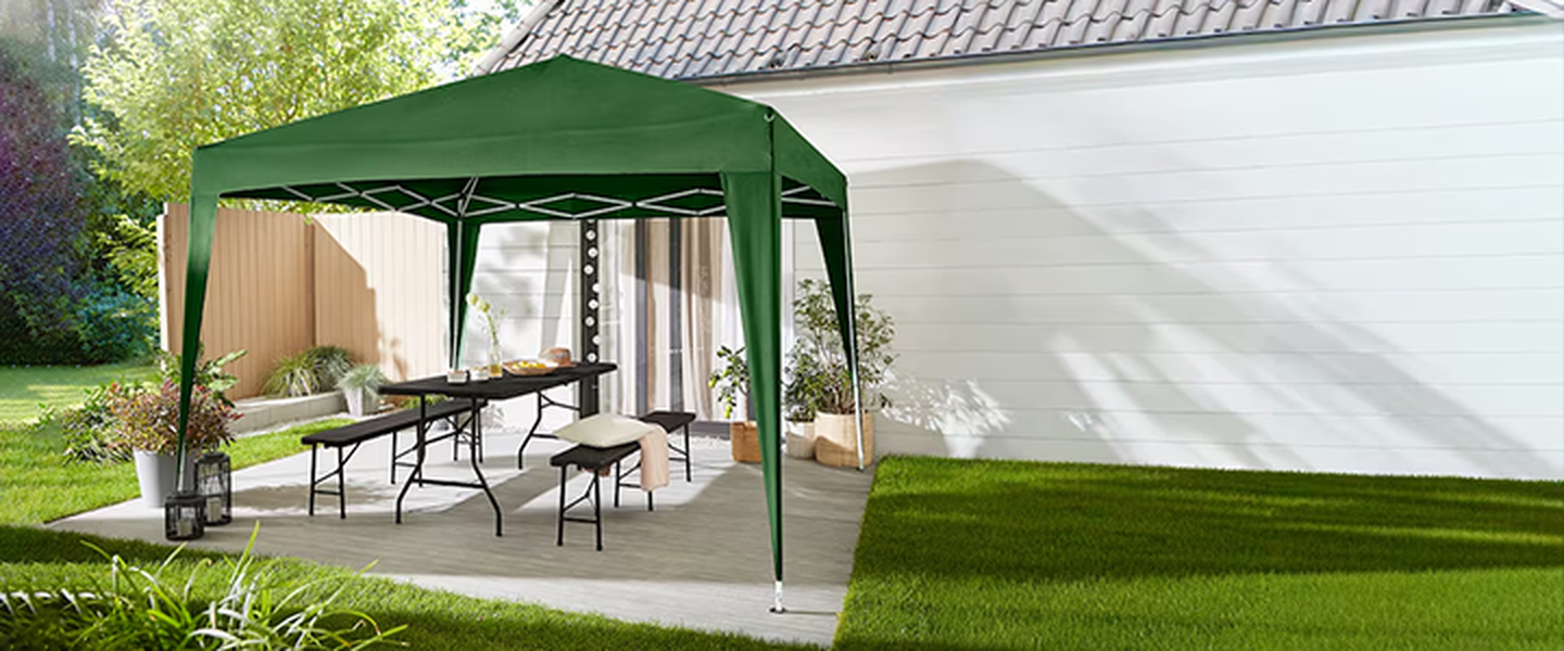 Terrasse im Freien mit grünem Pavillon, Holztisch, Bänken mit Kissen, umgeben von Pflanzen und Gras.