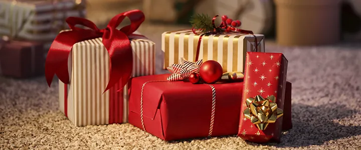 Festlich verpackte Geschenke mit roten und goldenen Bändern und Ornamenten, die auf einem Teppichboden platziert sind und eine warme Weihnachtsstimmung schaffen.