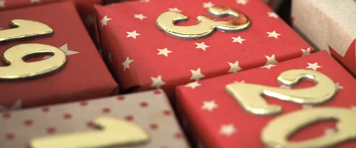 Nahaufnahme von rot-weißen, sternförmigen Geschenkboxen mit goldenen Zahlen darauf, die ein festliches und dekoratives Arrangement bilden.