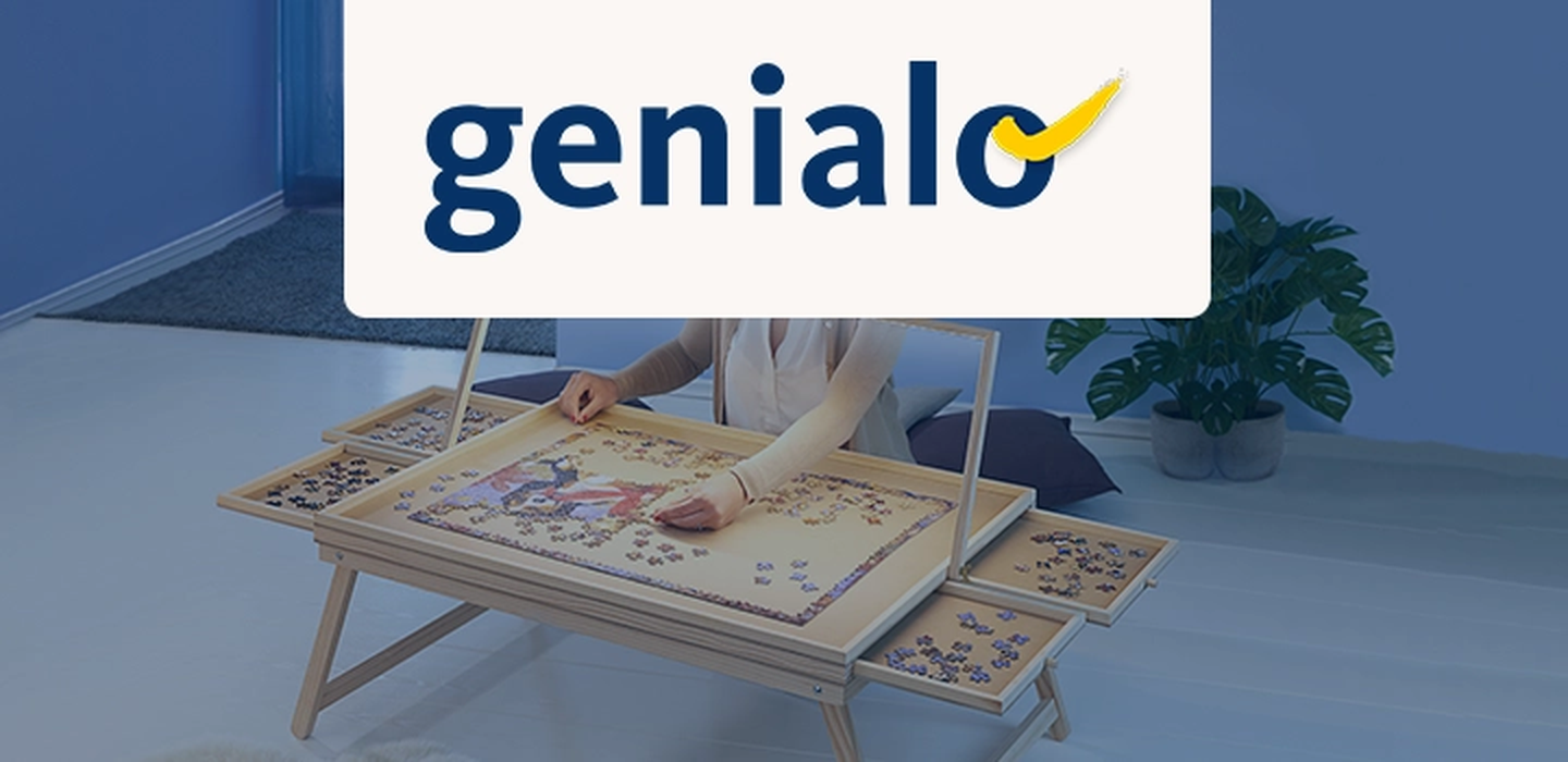 Person setzt ein Puzzle auf einem Holztisch mit seitlichen Erweiterungen zusammen, in einem blau getönten Raum mit einer Pflanze. „Genialo“-Logo oben.
