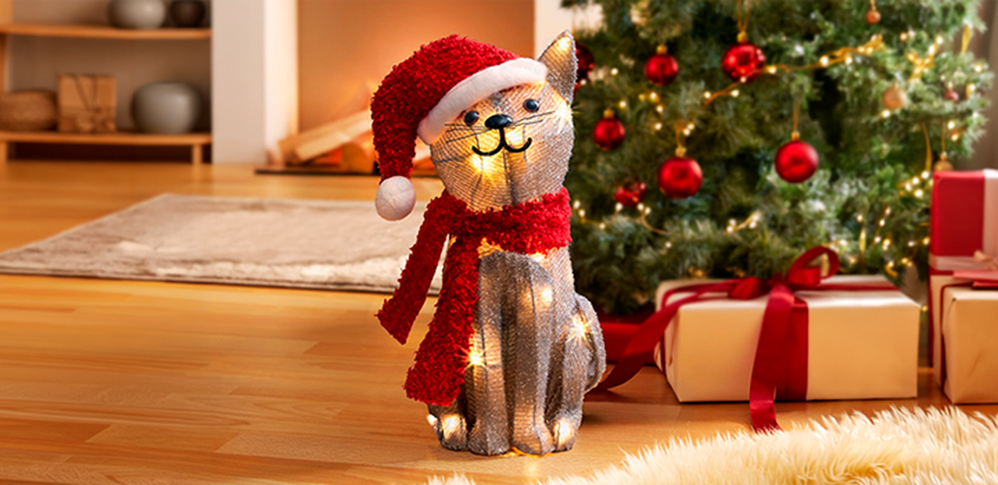 Beleuchtete Weihnachtskatze mit Mütze und Schal vor Weihnachtsbaum und Geschenken.