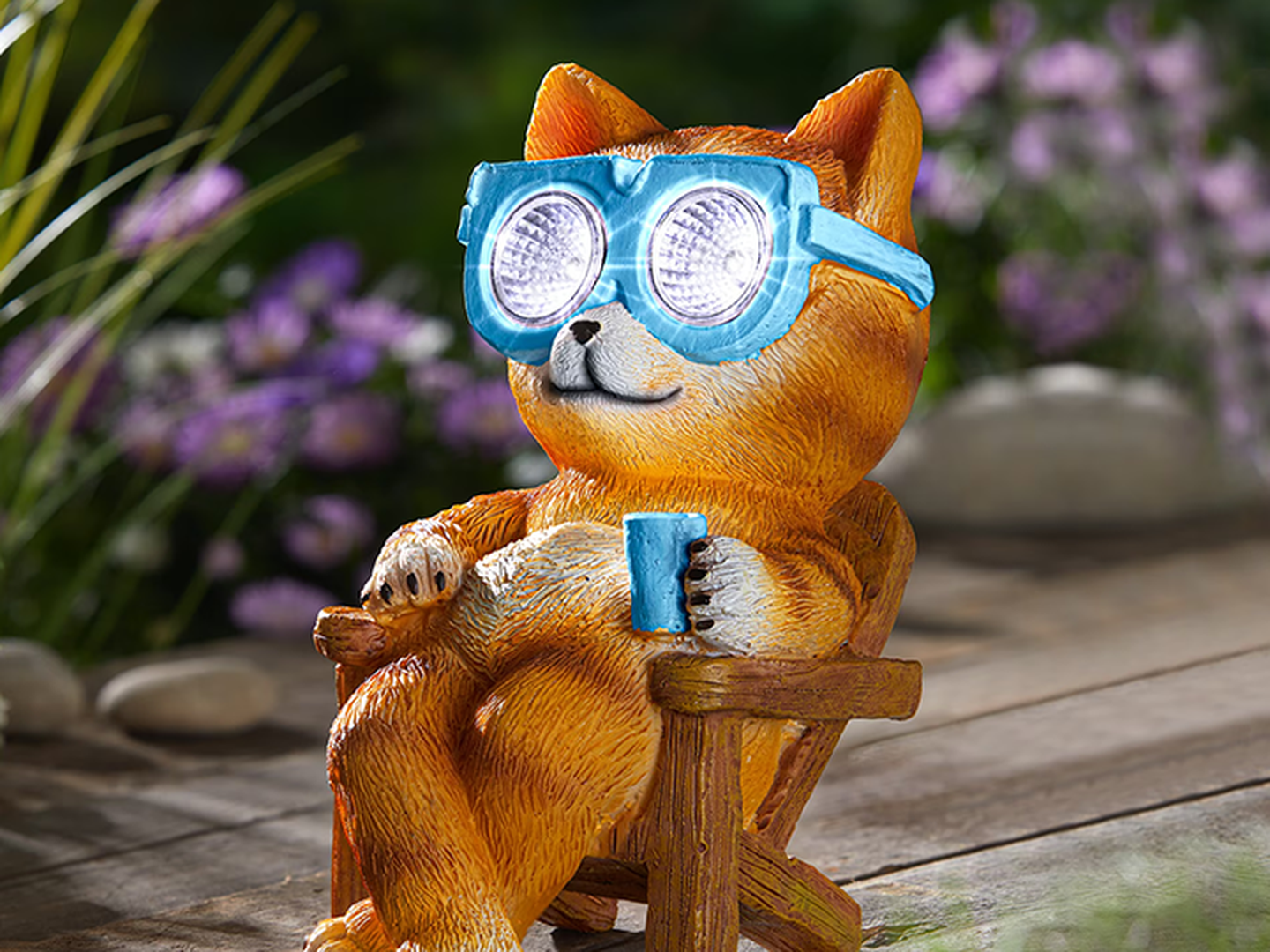 Eine niedliche Hundeskulptur mit blauer Brille entspannt sich in einem Sessel und hält eine Tasse in der Hand. Bunte Blumen und Grünpflanzen bilden den Hintergrund.