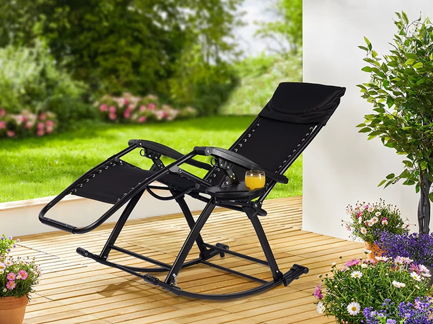 Schwarzer Liegesessel auf einer Holzterrasse, umgeben von üppigem Grün und Blumen.