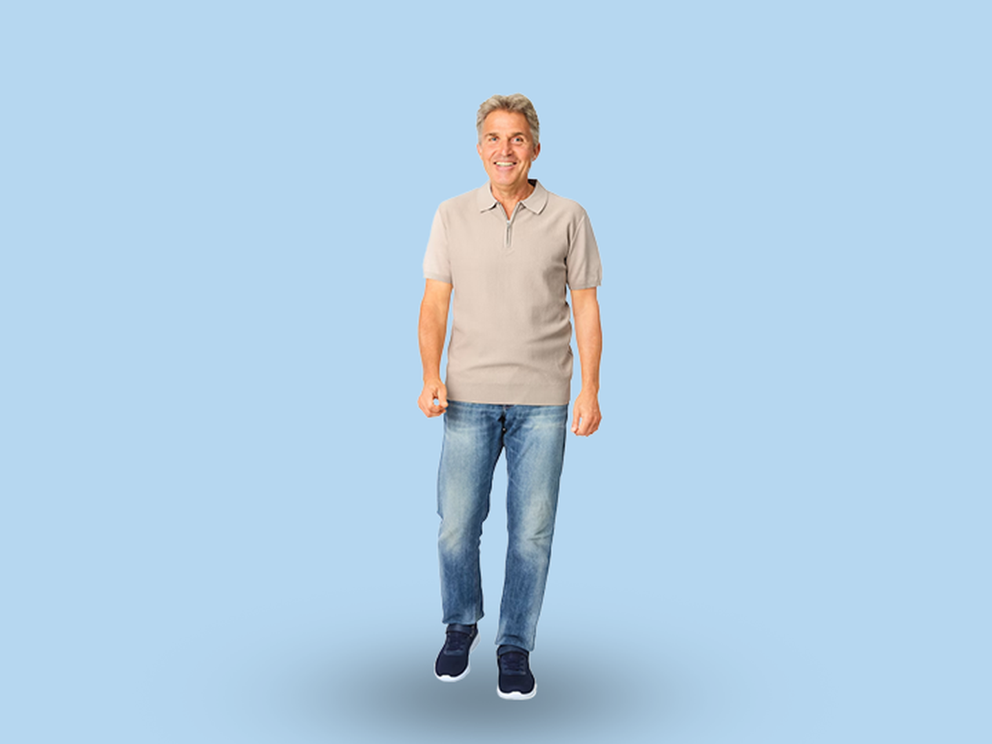 Ein lächelnder Mann in einem beigen Polohemd und Jeans steht vor einem hellblauen Hintergrund.