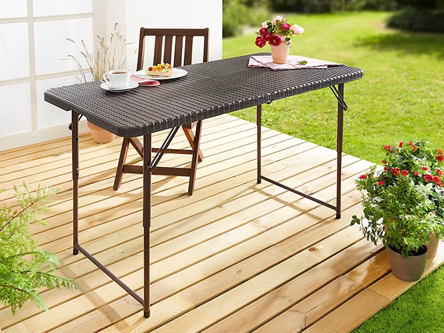 Terrasse im Freien mit einem Klapptisch, einem Holzstuhl, Topfpflanzen, einer Kaffeetasse und Gebäck.