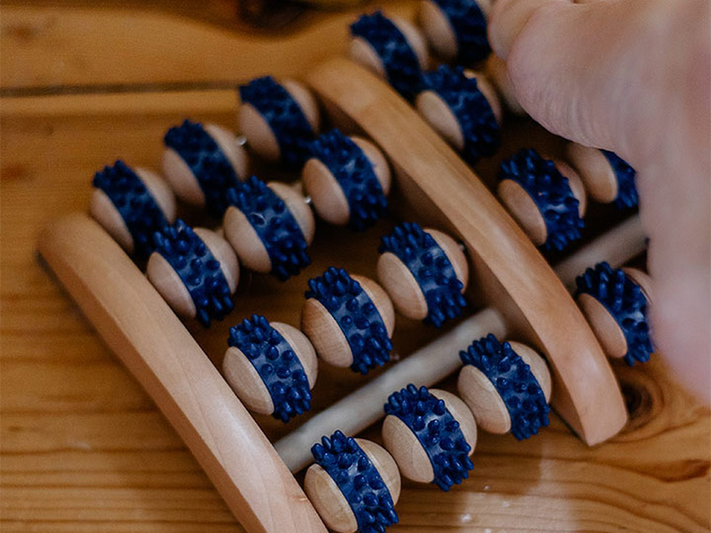 Hölzernes Fußmassagegerät mit Reihen blauer Stachelwalzen, das auf einem Holzboden verwendet wird.