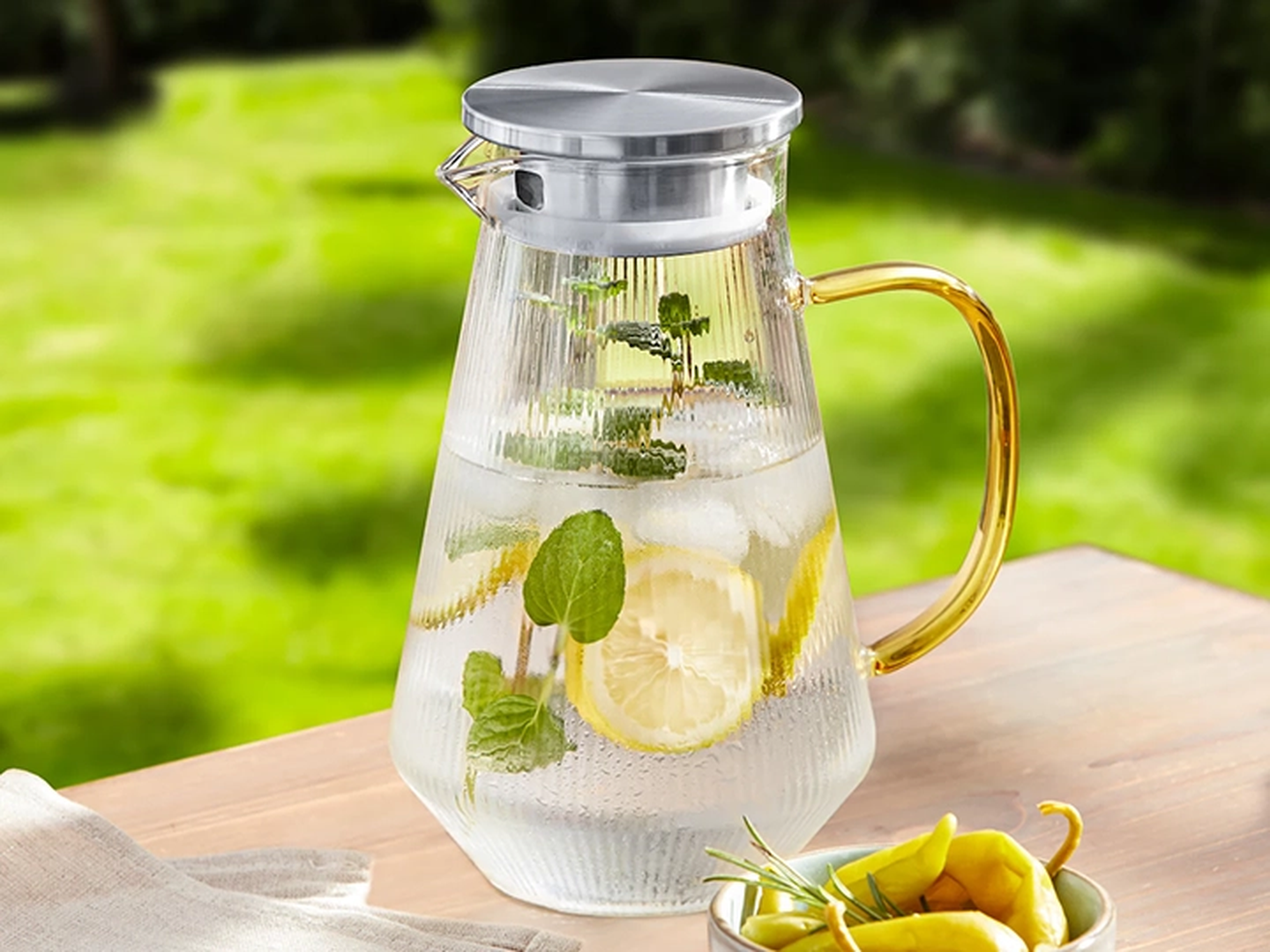 Ein Glaskrug mit Eiswasser, Zitronenscheiben und Minzblättern auf einem Holztisch.