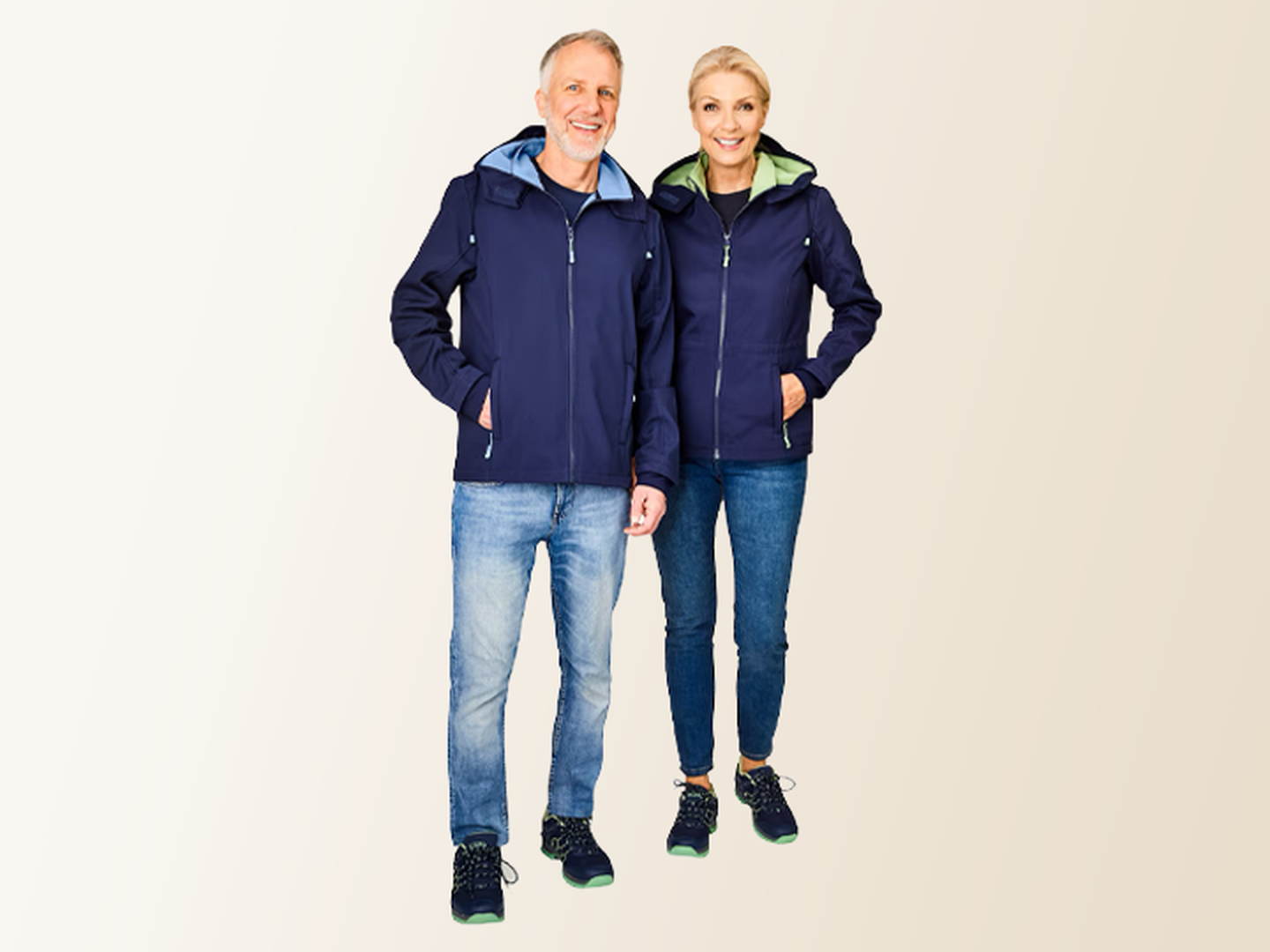 Ein lächelnder Mann und eine lächelnde Frau in passenden blauen Jacken und Jeans stehen vor einem hellen Hintergrund.