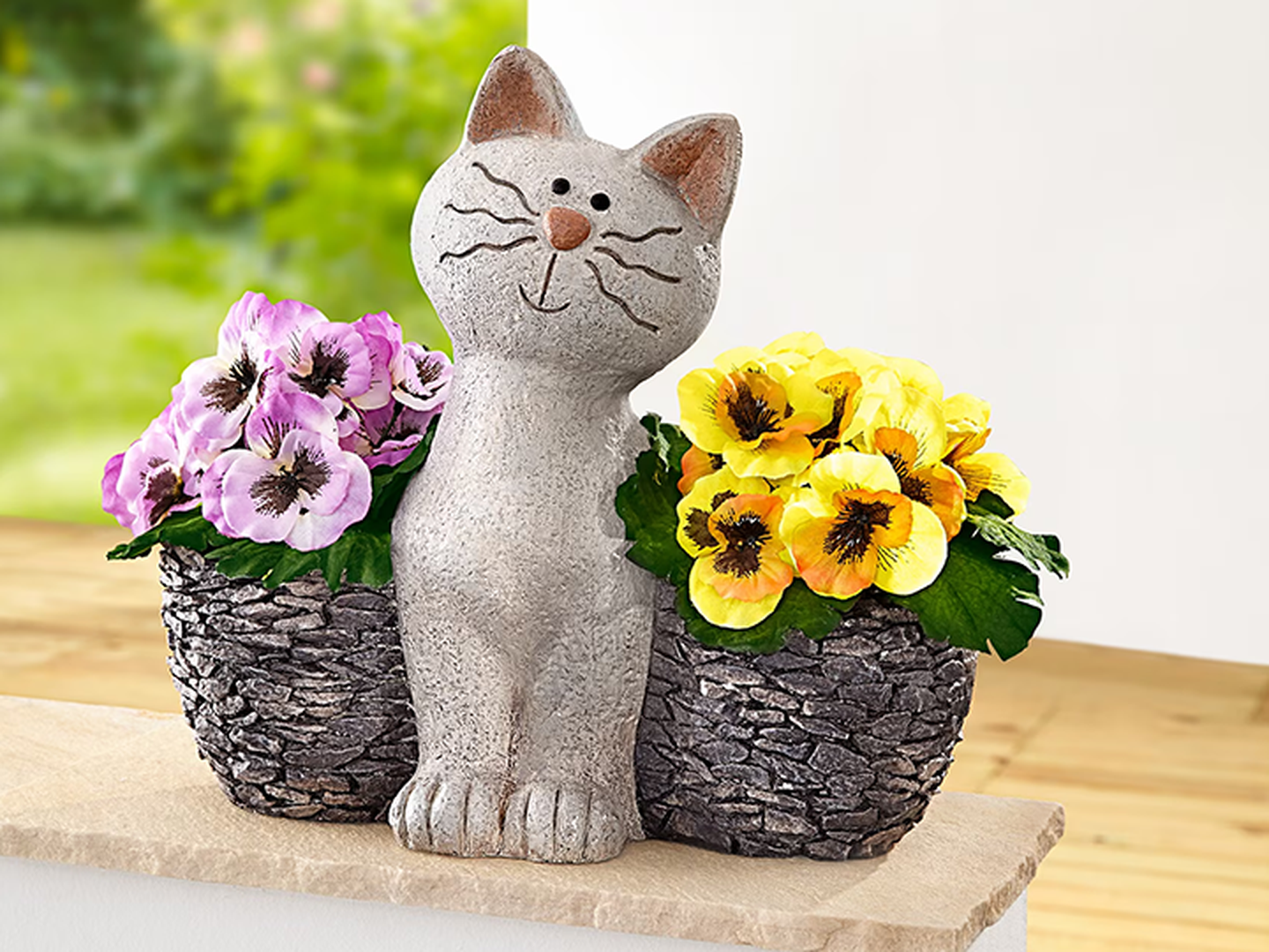 Eine steinerne Katzenstatue mit eingearbeiteten Details, platziert zwischen zwei Blumenkörben – einem mit violetten Blumen und einem mit gelben Blüten.