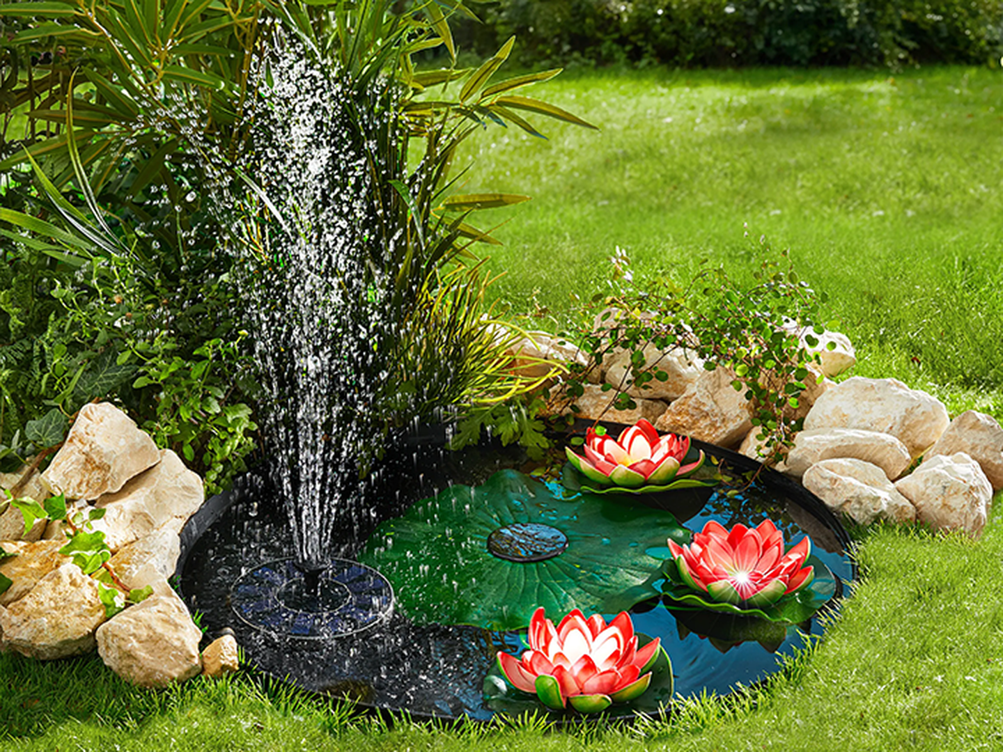 Kleiner Gartenteich mit Solar-Springbrunnen, umgeben von Steinen und Grün, mit leuchtend rosa Seerosen an der Wasseroberfläche.