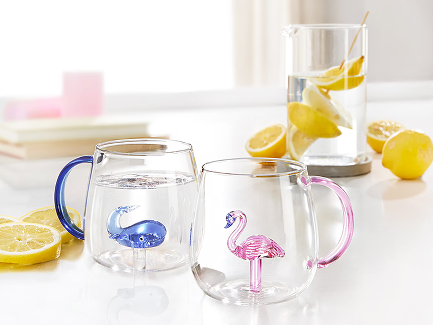 Zwei Glastassen mit bunten Tierfiguren im Inneren – eine blaue und eine rosa –, umgeben von Zitronenscheiben.