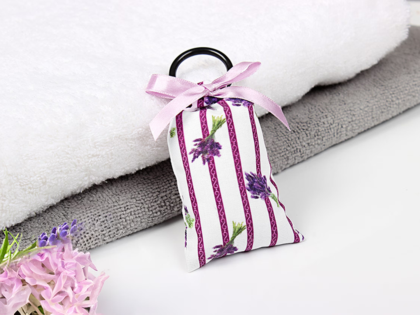 Ein gestreiftes Duftsäckchen mit lila schleife und Lavendel liegt auf einem Stapel Handtücher