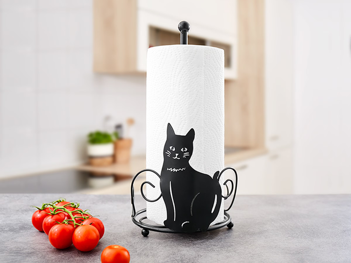 Ein Küchenrollenhalter mit einem Design einer schwarzen Katze auf einer Küchenarbeitsplatte, neben reifen Tomaten.