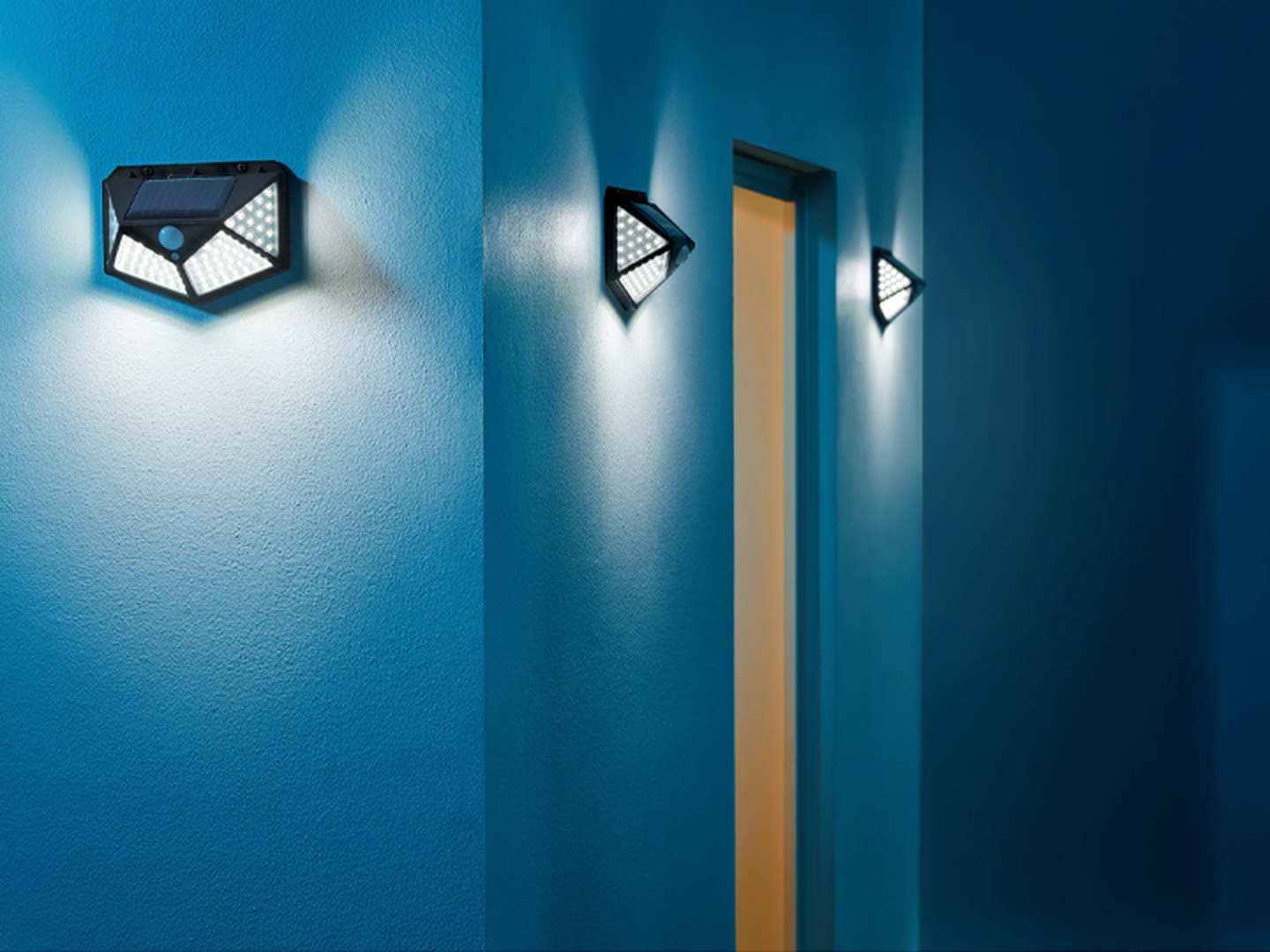 Ein blauer Flur mit zwei an der Wand montierten Solarleuchten neben einer offenen Tür, die ein warmes gelbes Licht ins Innere wirft.