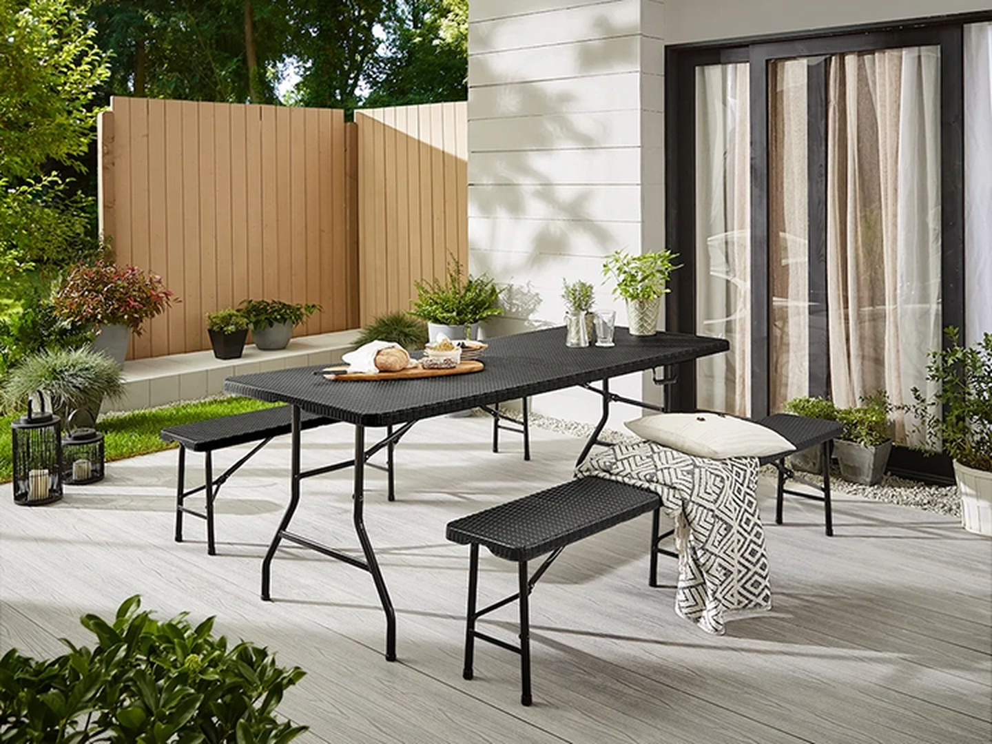 Eine Terrassengarnitur mit schwarzem Tisch und Bänken, umgeben von Pflanzen und einem Holzzaun, auf einer Terrasse.