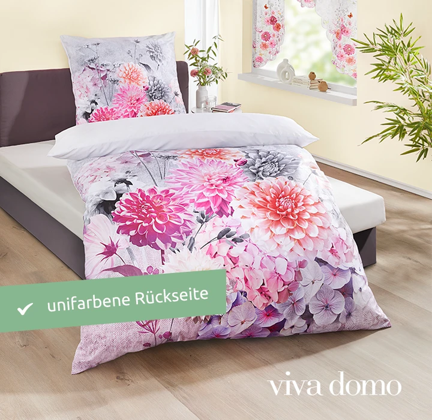 Bett mit Bettwäsche mit Blumenmuster in einem hellen Zimmer, mit großen Blumen in Rosa und Weiß. Helle Holzböden und eine Blattpflanze in der Nähe.