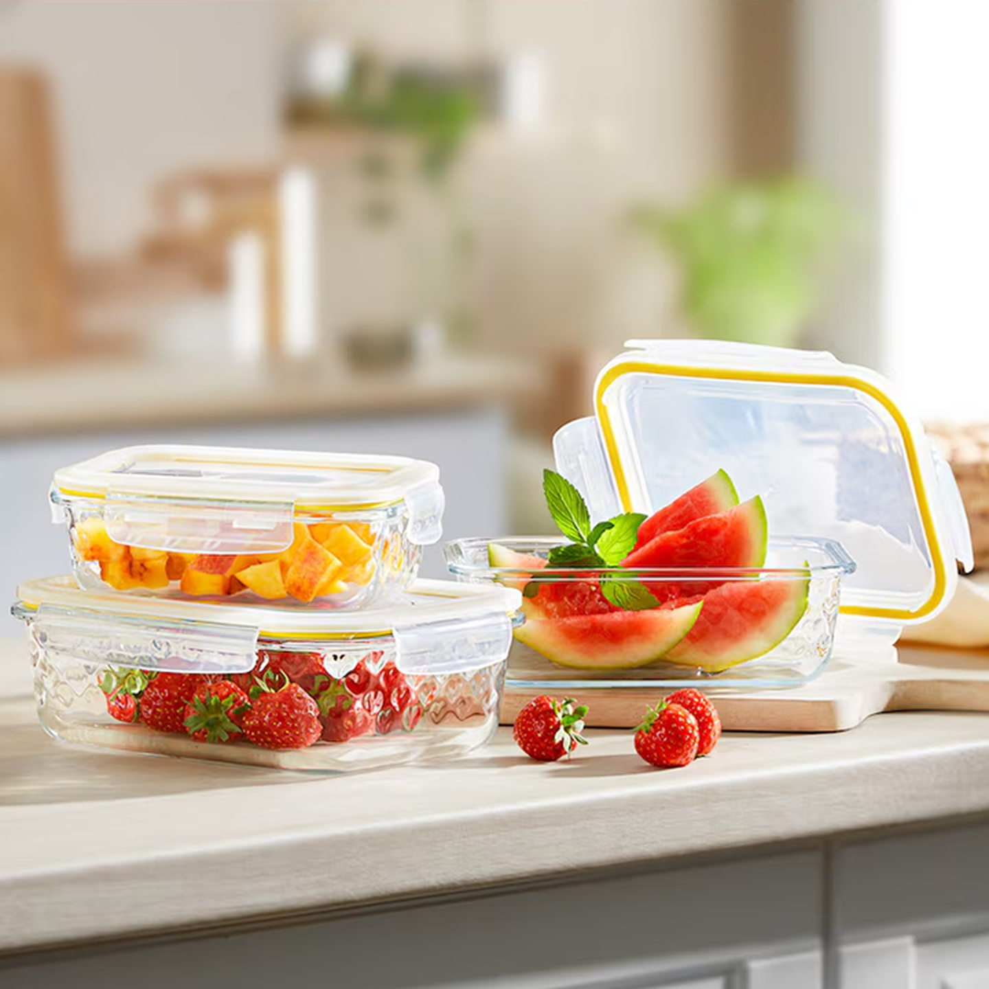 Glasbehälter mit geschnittenem Obst: Wassermelone, Erdbeeren und Mango, auf einer Küchentheke vor verschwommenem Hintergrund.