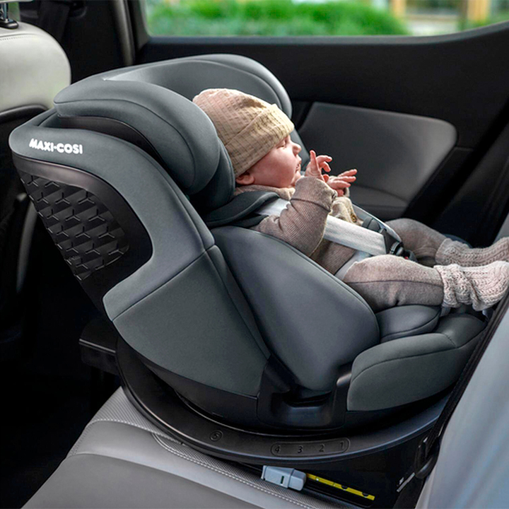 Baby in einem Autositz mit Mütze und Schühchen, mit Gurten gesichert, in rückwärtsgerichteter Position im Fahrzeug.
