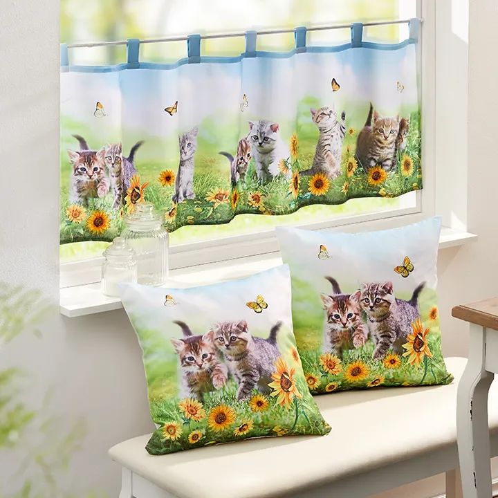 Vorhänge und Kissen mit verspielten Kätzchen, Sonnenblumen und Schmetterlingen, in einem hellen Raum mit einem Fenster und einer weißen Bank.