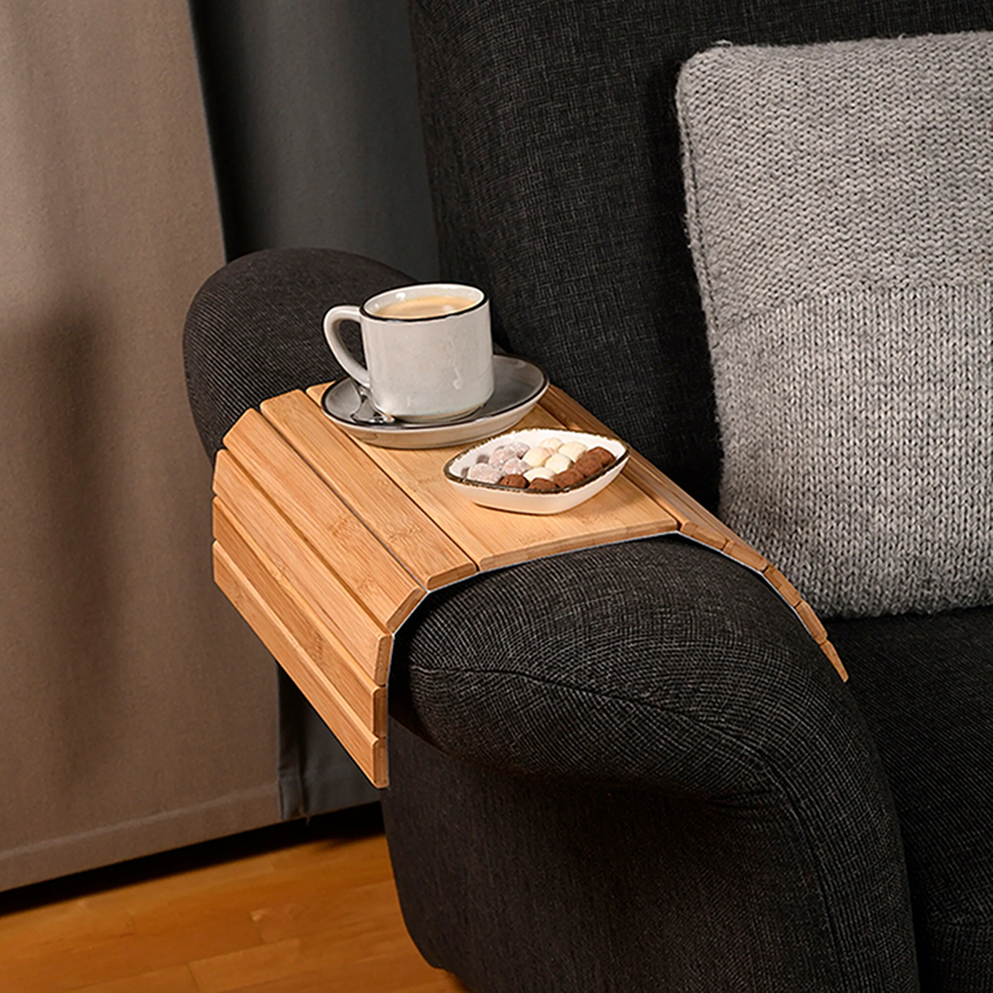 Auf einer Sofa Armlehne steht ein Bambus Sofatablett mit einer Tasse Kaffee und Kekse