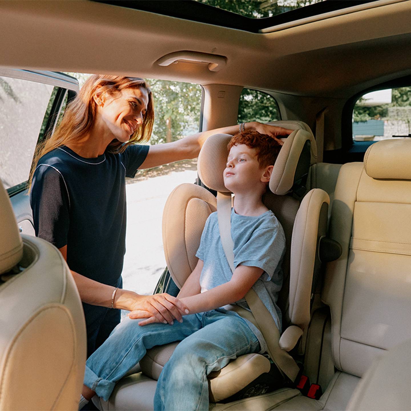 Eine Frau lächelt ein Kind an, das in einem CYBEX SOLUTION G2 I-FIX PLUS Autositz sitzt, und berührt sanft seinen Kopf.
