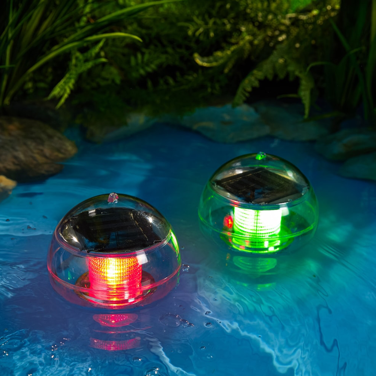 Zwei solarbetriebene Lichter schwimmen auf dem Wasser, eines leuchtet rot, das andere grün, umgeben von üppigem Grün.