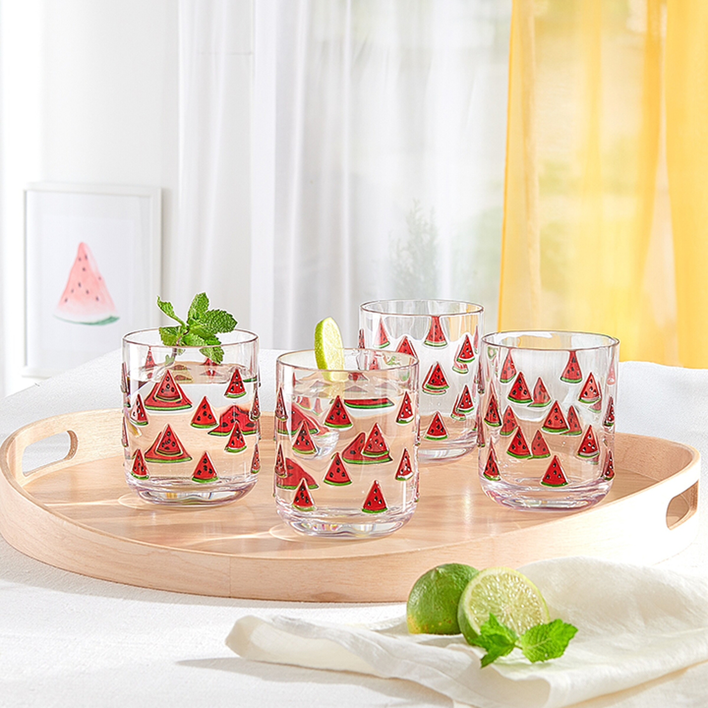 Vier mit Wassermelonenmustern verzierte Gläser, gefüllt mit Wasser und garniert mit Minze und Limette, sind auf einem runden Holztablett arrangiert. Limettenhälften und Minze liegen daneben.