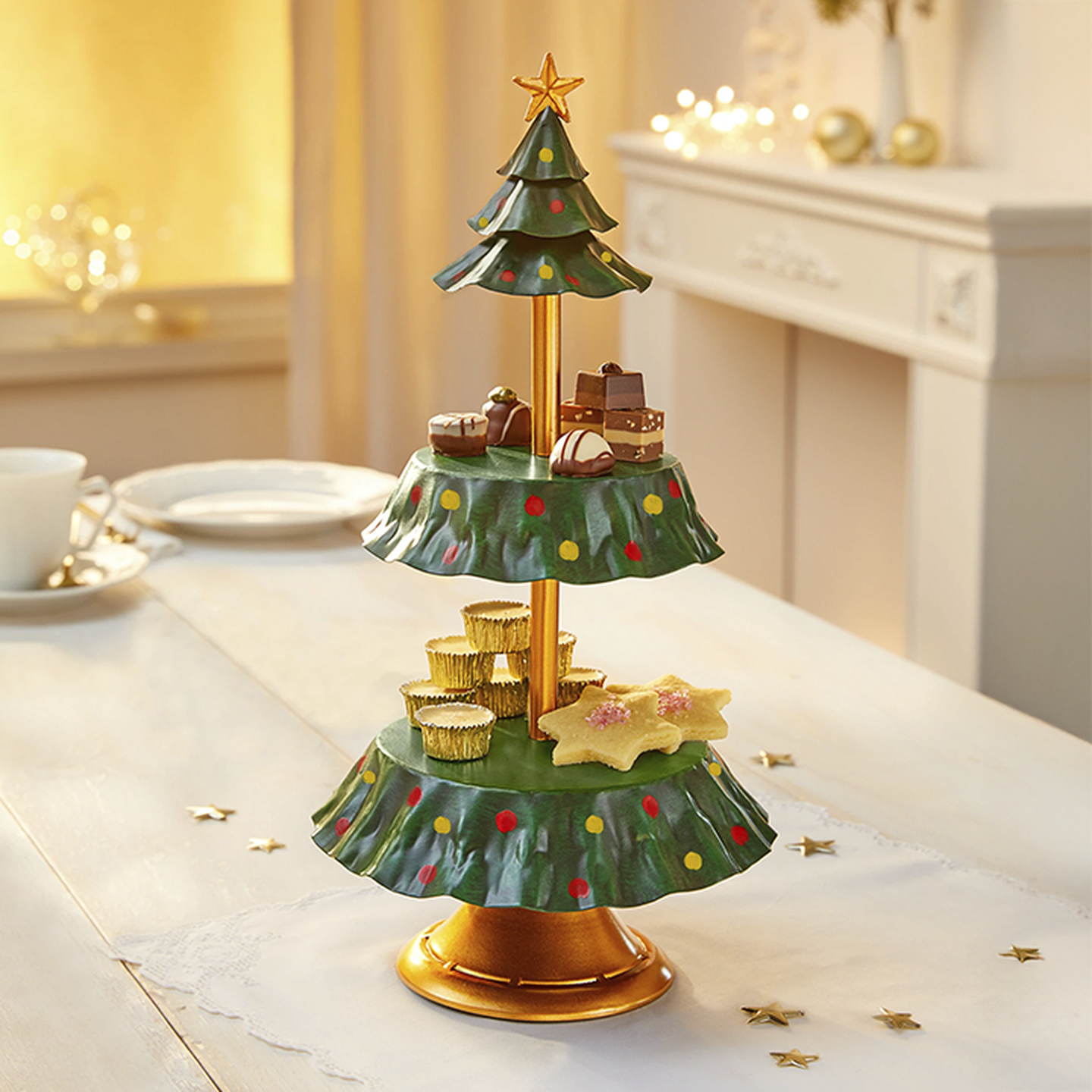 Festlicher zweistöckiger Ständer in Form eines Weihnachtsbaums mit Pralinen, Keksen und einer Sternspitze auf einem weißen Tisch in einem warm beleuchteten Raum.