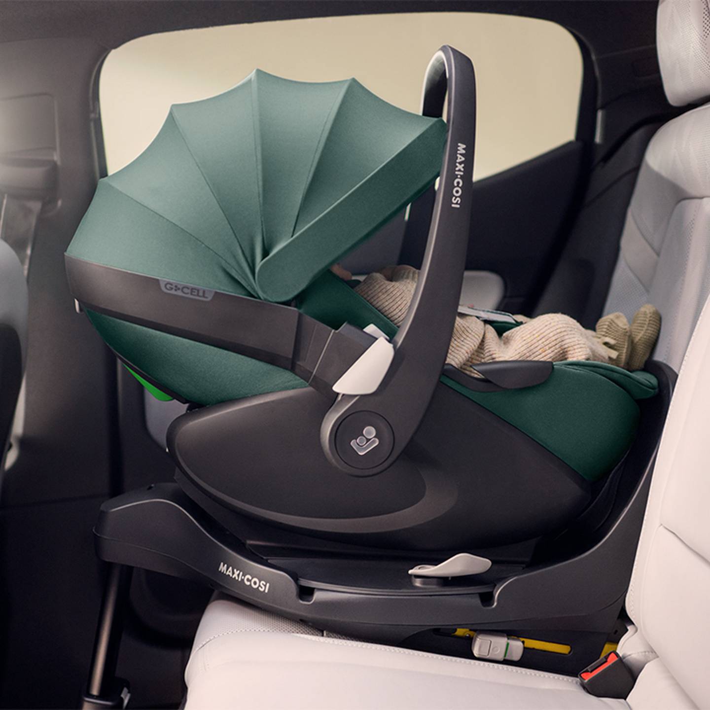 Rückwärtsgerichteter grüner Maxi-Cosi-Babysitz mit Verdeck, sicher auf dem Rücksitz eines Autos mit einem eingewickelten Baby installiert.