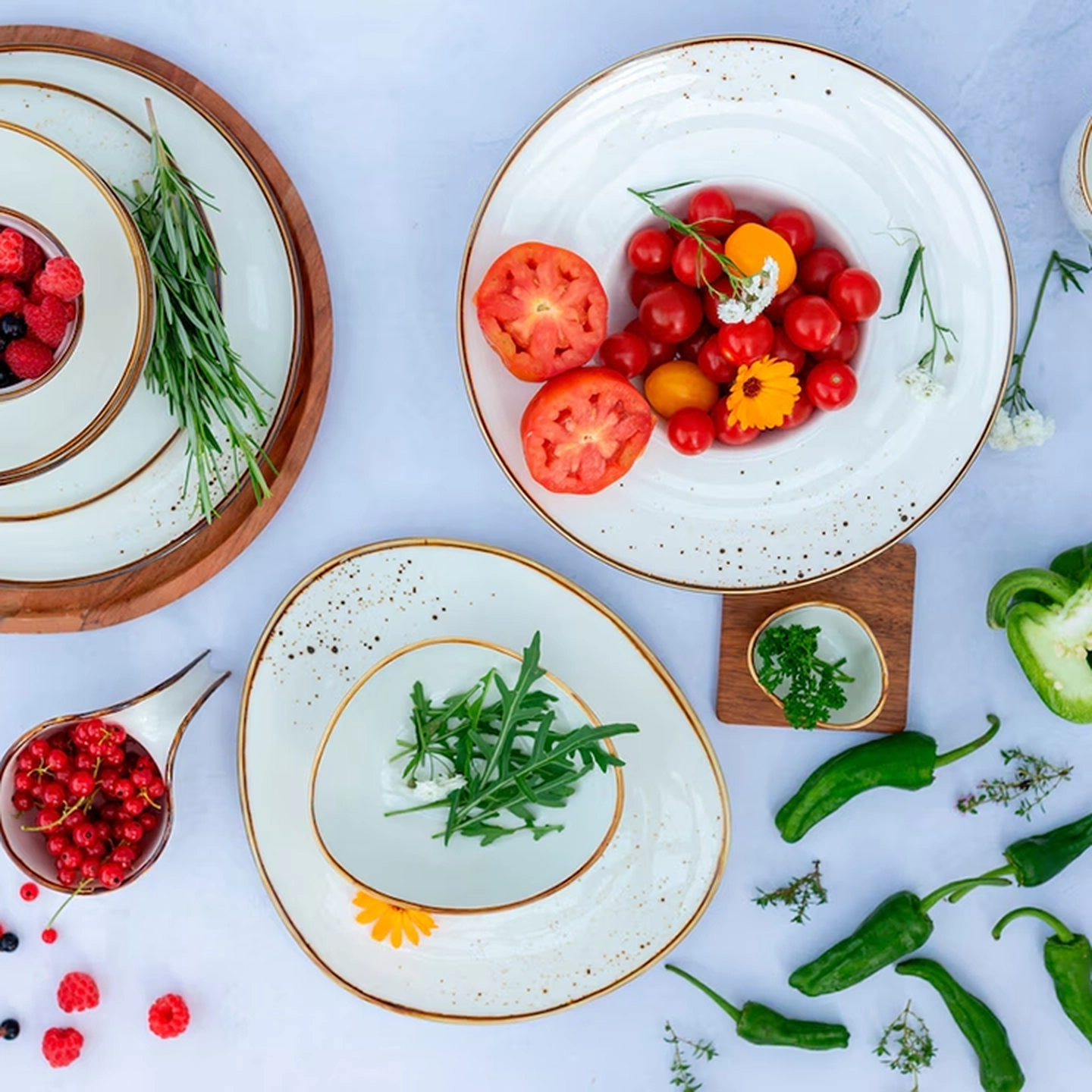 Verschiedene frische Gemüsesorten, Beeren und Kräuter sind kunstvoll auf eleganten, gesprenkelten weißen Tellern auf einer weißen Oberfläche arrangiert.